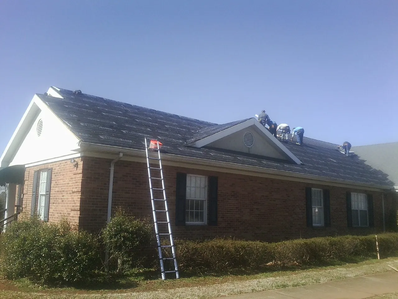 Crew tearing shingles off a brick ranch roof with a ladder set — Emergency Roof Repair work by our crew in Moses Lake