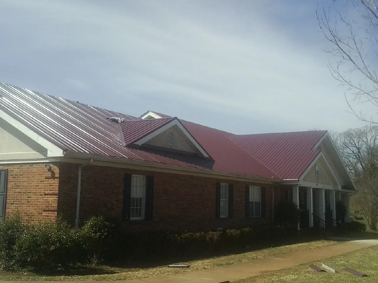 Red metal roof with gabled entries on a long brick building, from a Hail Damage Roof Repair job in Moses Lake