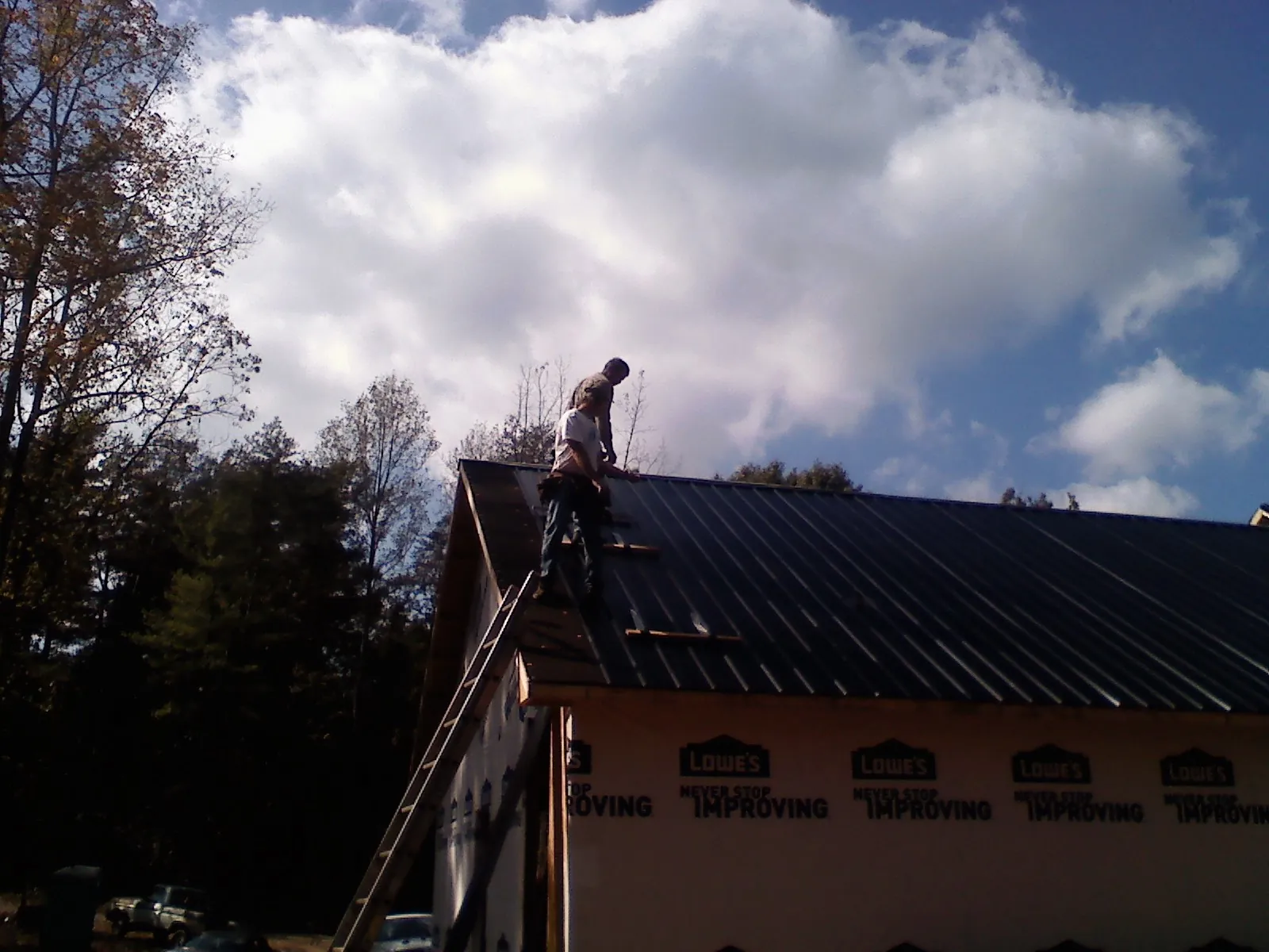Roofer fastening dark metal panels high against a cloudy sky, from a Roof Inspection job in Moses Lake