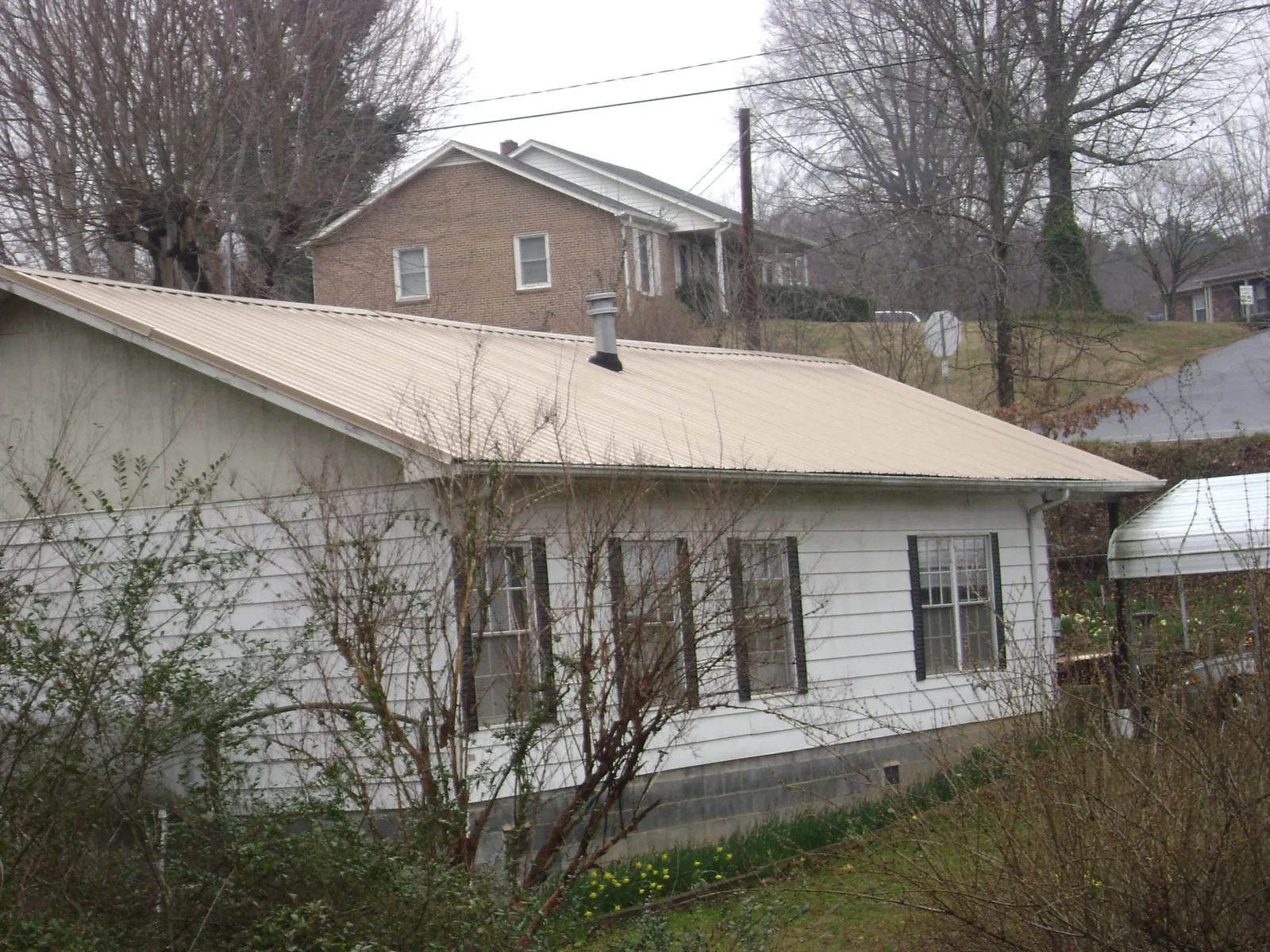 Tan metal roof on a white sided house set into a hillside — Commercial Roofing by Roofing Brothers in Moses Lake